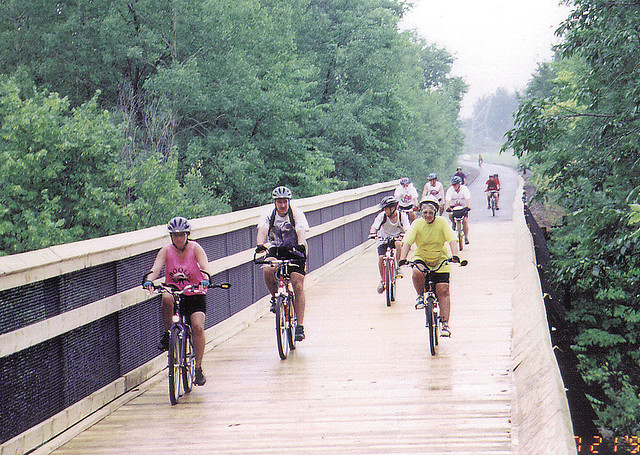 Cyclists enjoy a ride on a scenic wood bridge surrounded by lush greenery.
