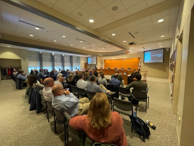 People attending a seminar in a conference room with a presenter speaking at a podium.