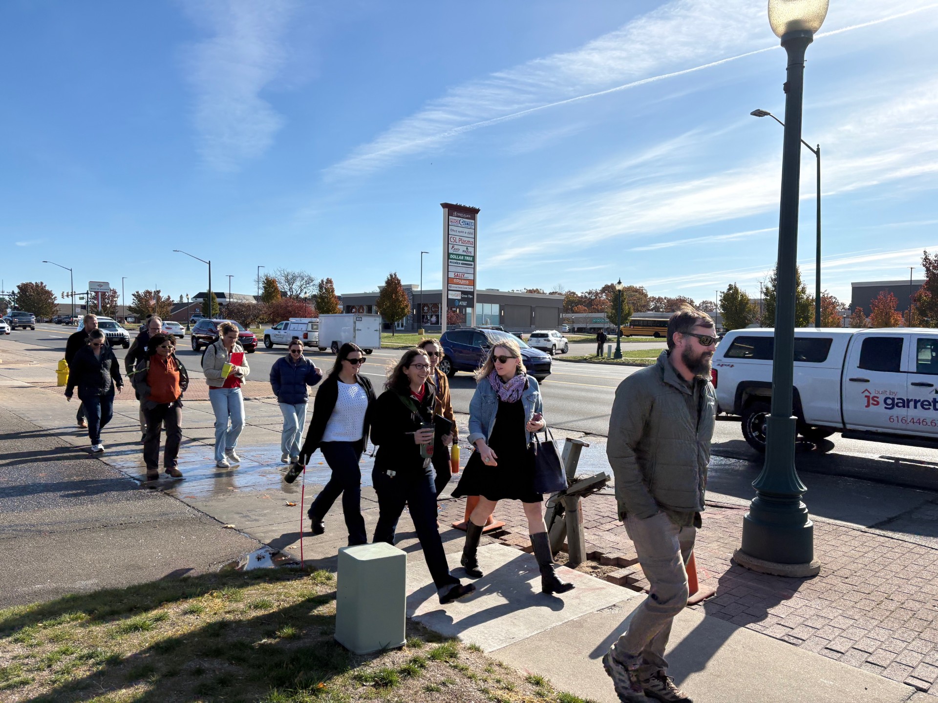 People walking on a sidewalk near a busy street under a clear blue sky.
