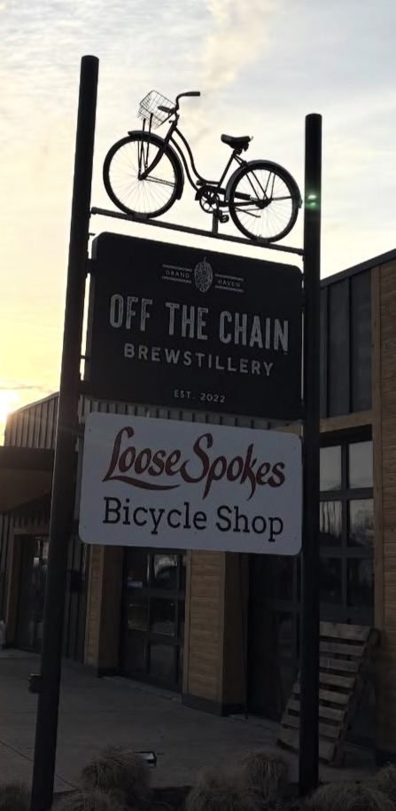 Bicycle atop sign for Off the Chain Brewstillery and Loose Spokes Bicycle Shop at sunset.