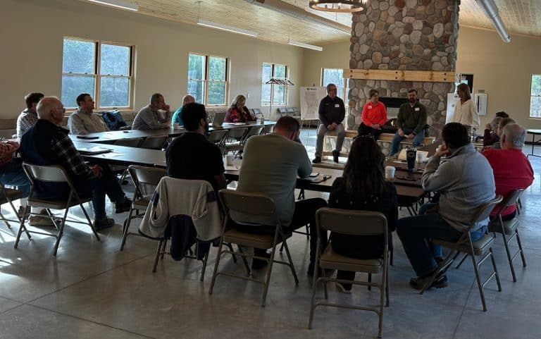 Group attending a workshop in a bright room with stone fireplace, engaging in discussions at a long table.