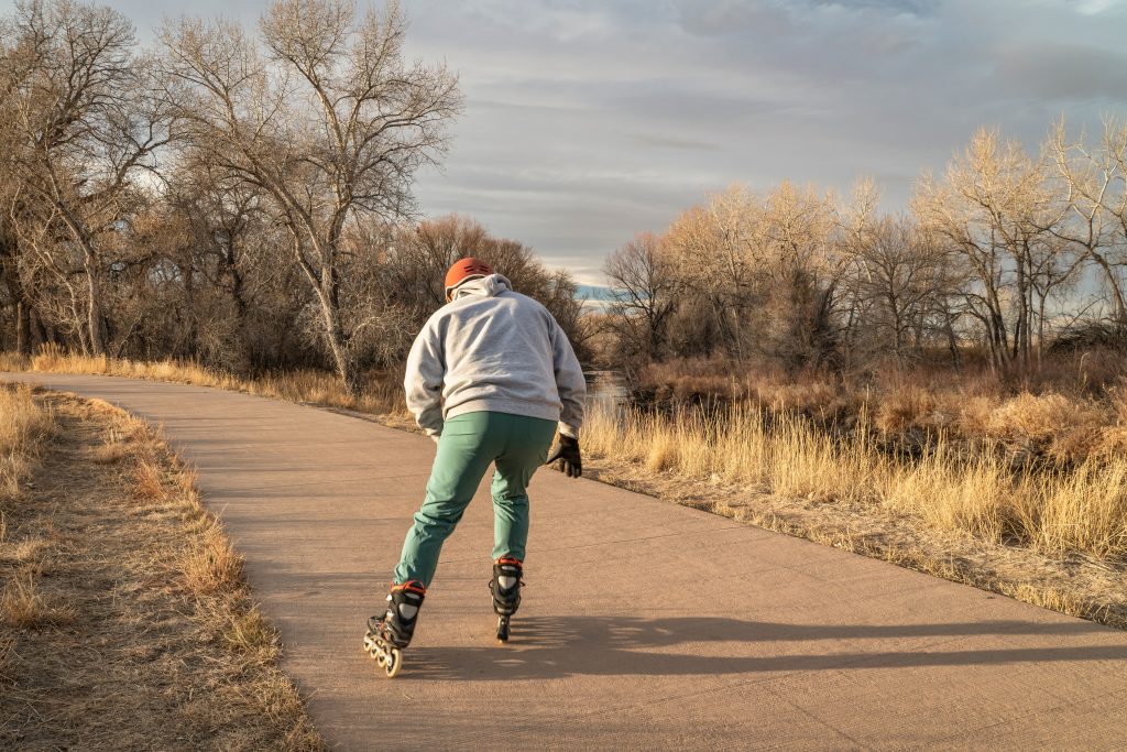 Rollerblading on a scenic autumn path with trees and a clear sky, wearing protective gear and enjoying the outdoors.