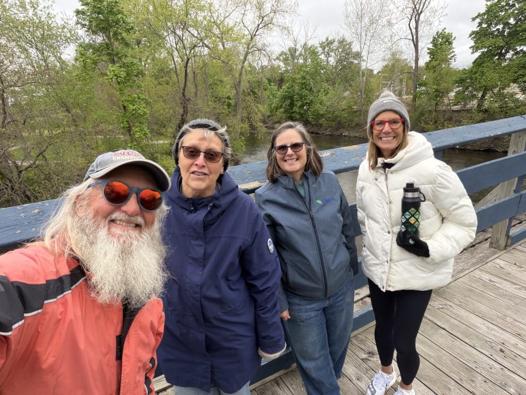 Group of friends enjoying a walk on a wooden bridge surrounded by lush greenery and a river in the background.